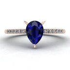 Front studio hero shot of the Calista engagement ring, featuring a prominent pear-shaped blue sapphire on a rose gold band with sparkling white diamond shoulders.