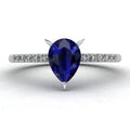 Front view of the Calista engagement ring, showcasing a prominent pear-shaped blue sapphire on a polished white gold or platinum band with diamond shoulders.