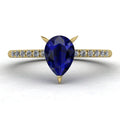 Calista engagement ring, showcasing a prominent pear-shaped blue sapphire on a polished yellow gold band with diamond shoulders.