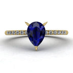 Calista engagement ring, showcasing a prominent pear-shaped blue sapphire on a polished yellow gold band with diamond shoulders.