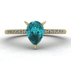 Hero shot of the Calista 18ct yellow gold ring, featuring a rich pear-shaped teal sapphire surrounded by a halo of white diamonds.