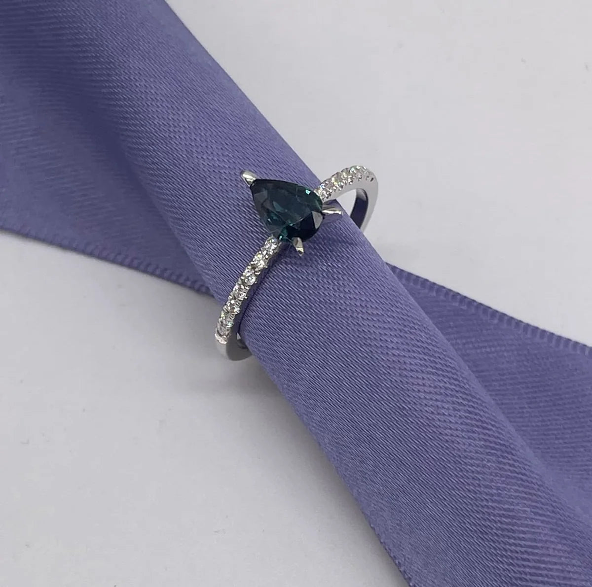 Calista pear shaped teal sapphire and diamond engagement ring in 18ct white gold, front view showing the vivid teal sapphire and diamond shoulders, handmade in our London studio