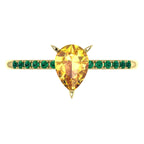 Top-down hero shot of the Calista 18ct yellow gold ring, featuring a vibrant pear-shaped yellow sapphire framed by a halo of lush green emeralds