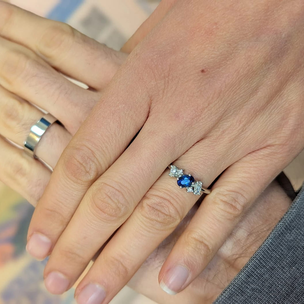 Client wearing the Atlantis blue sapphire and diamond asymmetrical cluster engagement ring in white gold, shown on hand