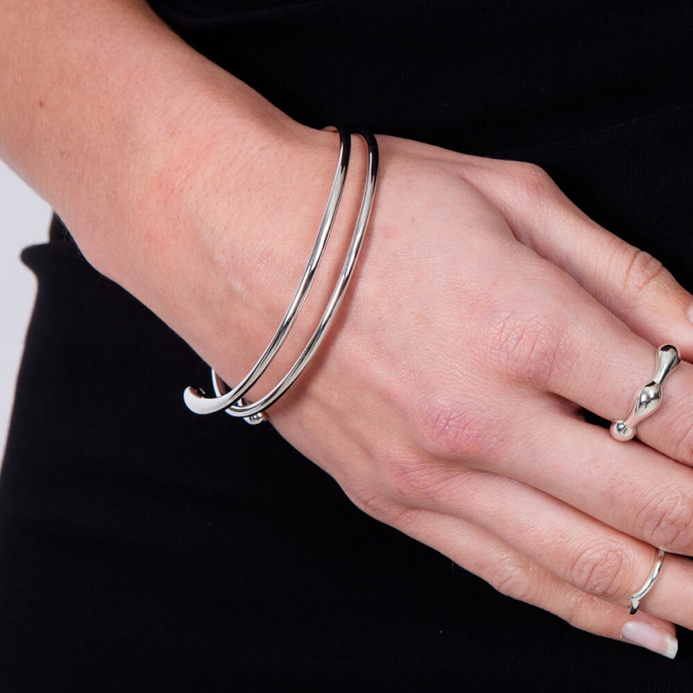 Coil Drip Bangle worn on model's wrist stacked with Drip Collection rings — polished sterling silver double coil bangle