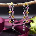 lifestyle view of the double-drop earrings, highlighting the sparkle of the diamonds and gemstones hanging on a branch.