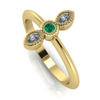 Angled perspective of an 18ct yellow gold trilogy ring with an emerald and diamonds featuring fine milgrain textured edges.