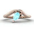 Enchanted pear shaped aquamarine asymmetric solitaire engagement ring in rose gold, front view showing icy blue stone and sculptural sweeping band