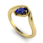 Enchanted pear blue sapphire engagement ring in yellow gold, three-quarter angle view showing vivid blue stone nestled in asymmetric wrapped setting
