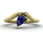 Enchanted pear shaped blue sapphire asymmetric solitaire engagement ring in yellow gold, front view showing deep blue stone and sculptural sweeping band