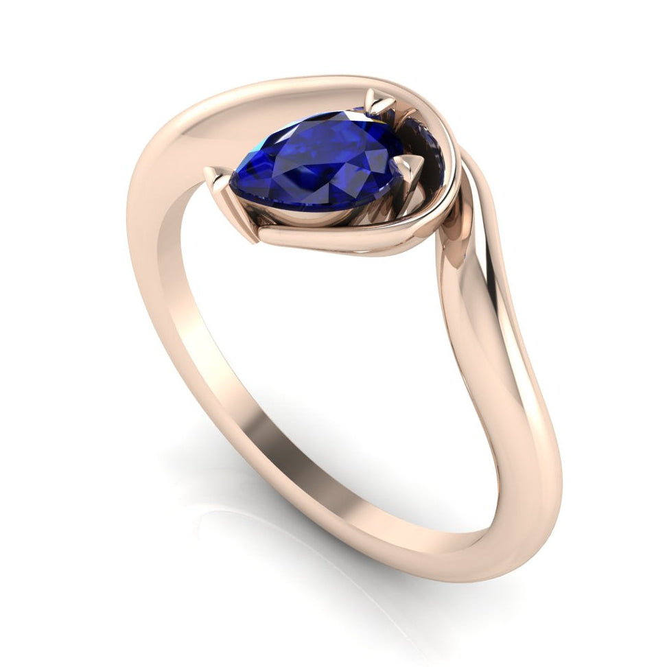 Enchanted pear sapphire engagement ring in rose gold, three-quarter angle view showing vivid blue stone and fluid asymmetric wrapped setting