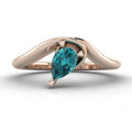 Enchanted pear shaped teal sapphire asymmetric solitaire engagement ring in rose gold, front view showing vivid blue-green stone and sculptural sweeping band