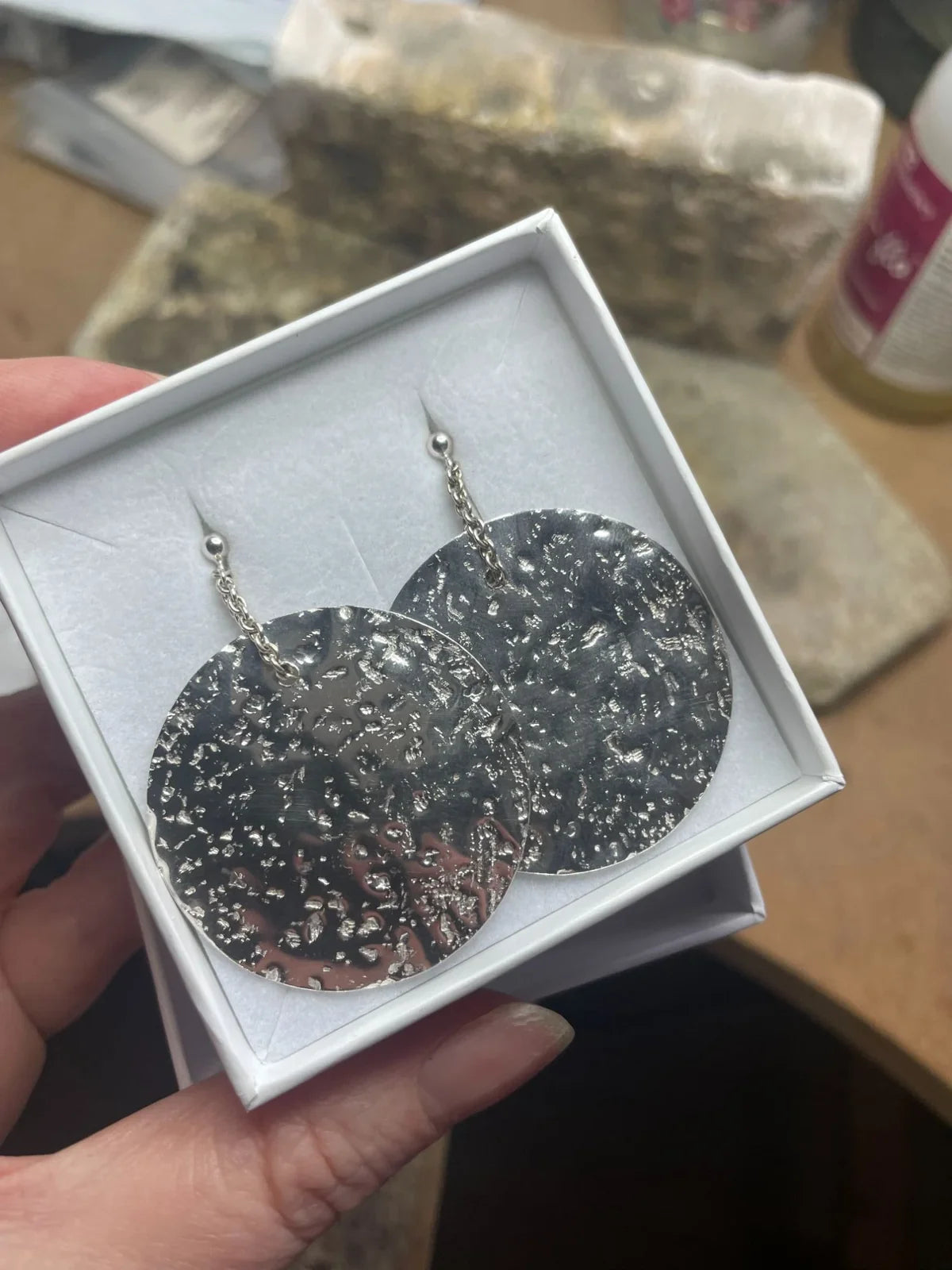 Pair of medium Glitter Ball recycled silver disc earrings presented in a white gift box, held by hand in the London studio