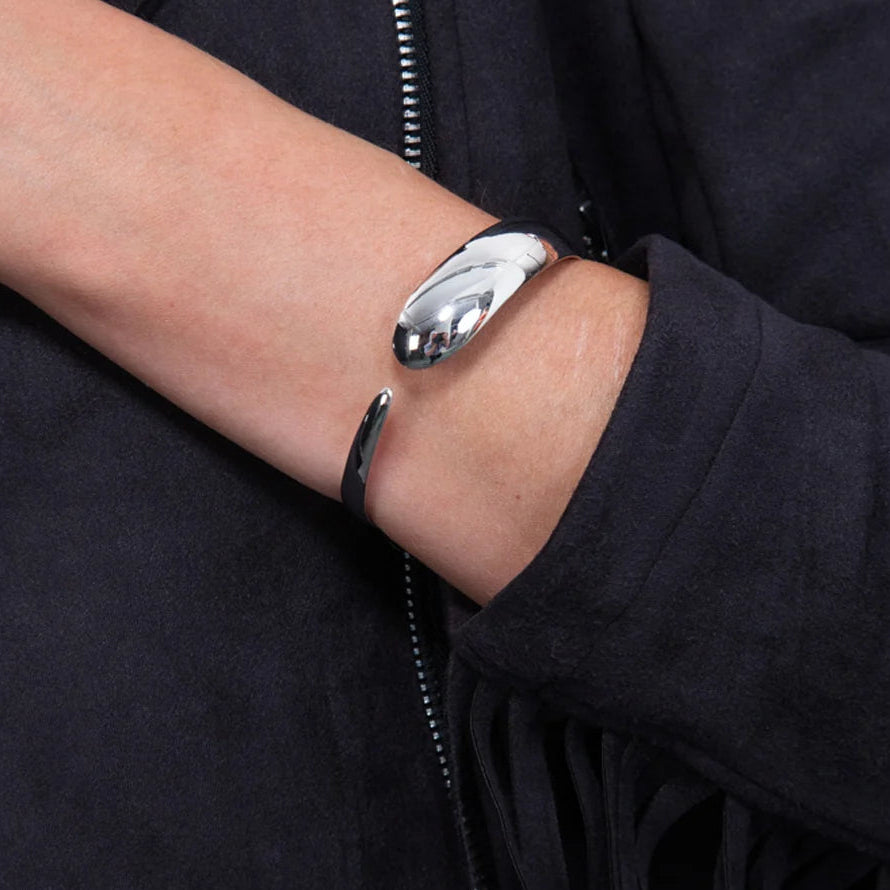 Flat Drip Silver Bangle in sterling silver — model wearing cuff on wrist against dark jacket, showing the bold domed front