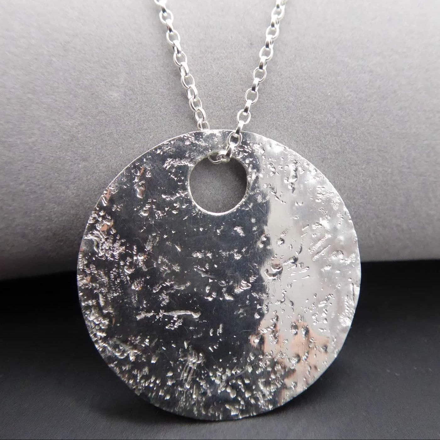 Silver textured handmade glitter ball pendant necklace on a grey surface