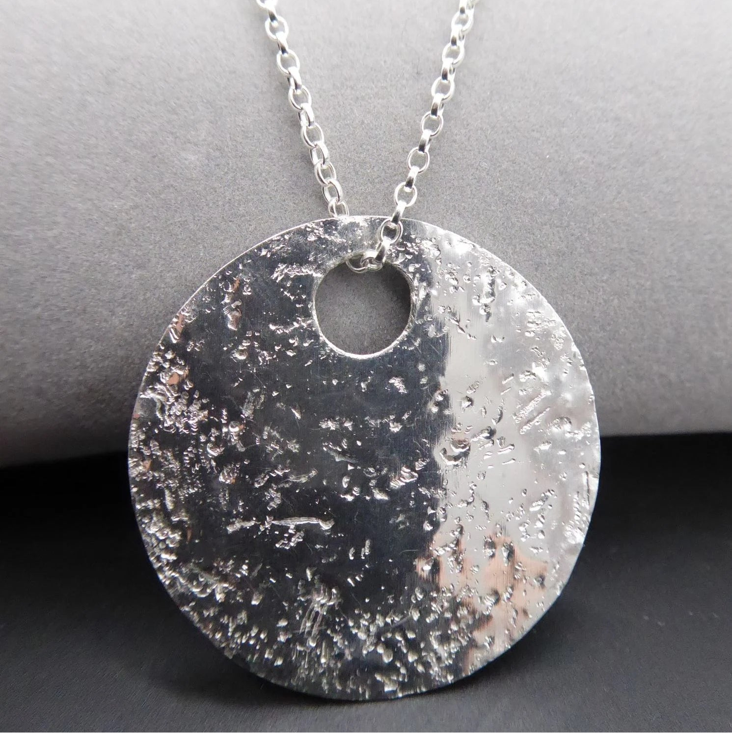 Silver textured handmade glitter ball pendant necklace on a grey surface