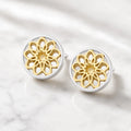 Front view of gold and silver mandala stud earrings with intricate openwork floral patterns on a cream background.