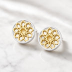 Front view of gold and silver mandala stud earrings with intricate openwork floral patterns on a cream background.