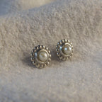 Pair of pearl and silver earrings on a textured grey surface