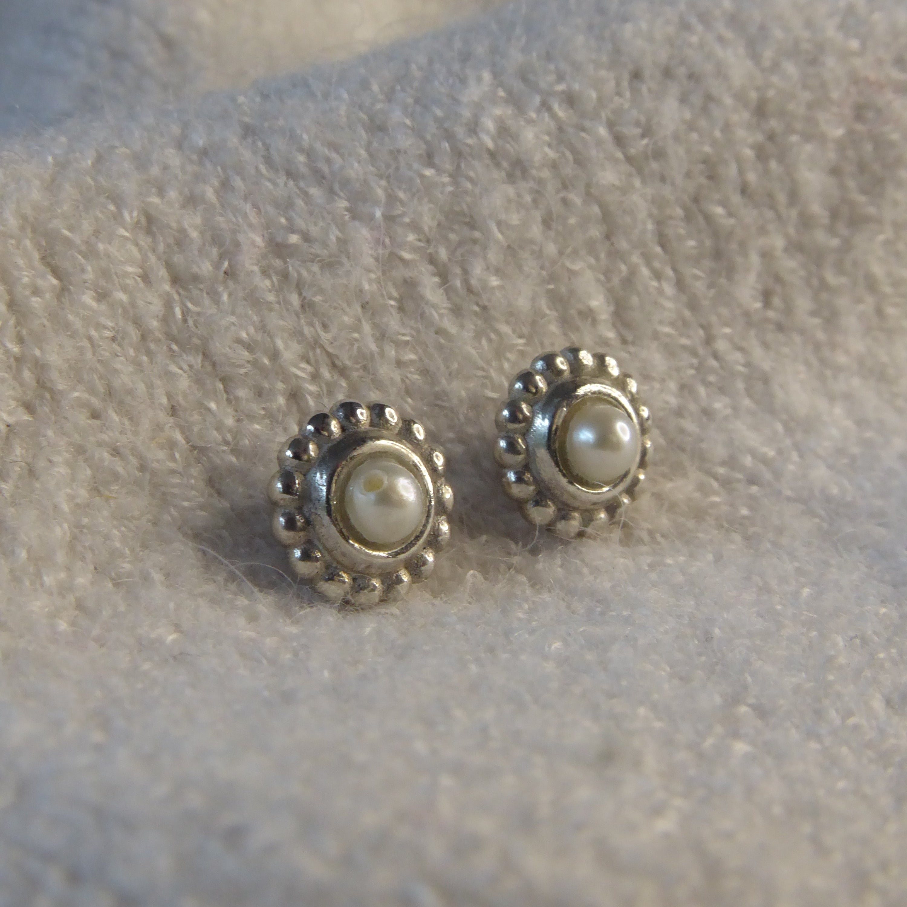 Pair of pearl and silver earrings on a textured grey surface