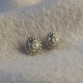 Ivory freshwater pearl and recycled silver Mini Alto stud earrings laid on a textured cream surface, showing millgrain beaded border detail
