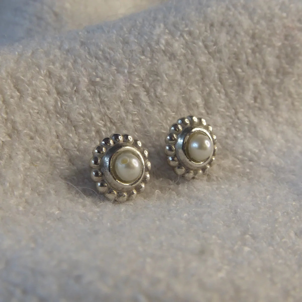 Ivory freshwater pearl and recycled silver Mini Alto stud earrings laid on a textured cream surface, showing millgrain beaded border detail