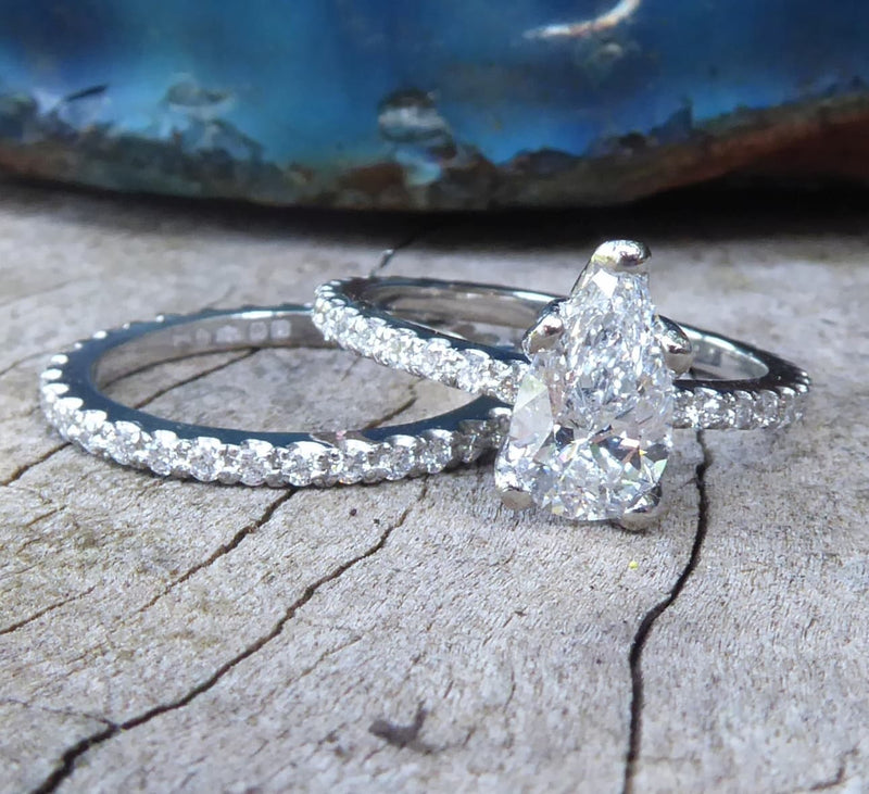 Two bespoke matching diamond rings, a wedding and engagement ring on a textured surface with a blurred natural background