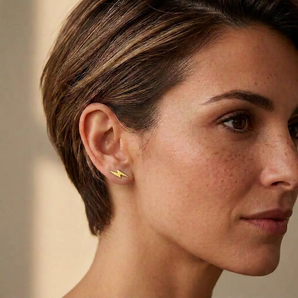 Gold-plated lightning bolt stud earring worn on a model's earlobe, showing its dainty size. Side view