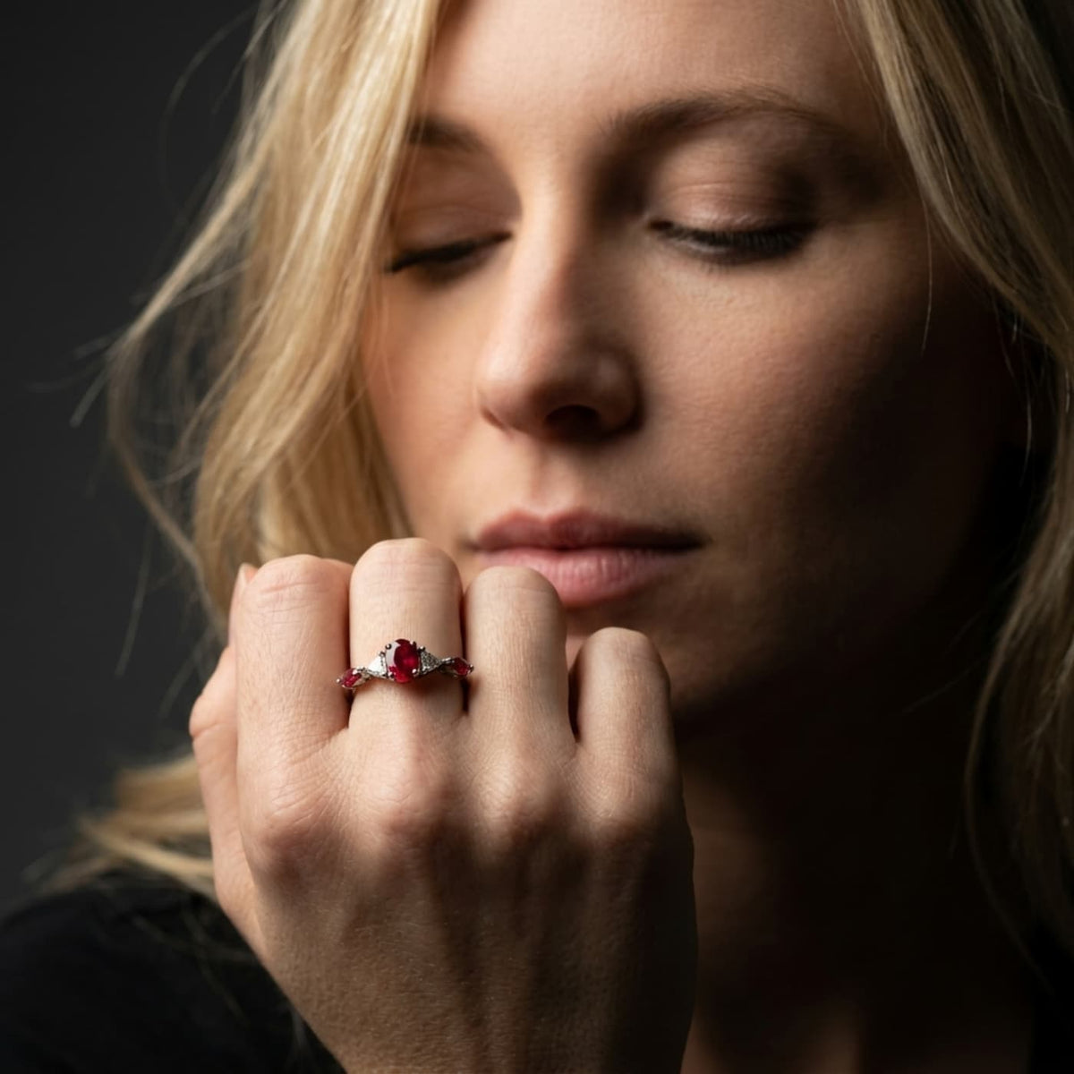 Maisie oval ruby and diamond engagement ring worn on hand in 18ct white gold, showing the vivid oval ruby centre stone with diamond shoulders, handmade in our London studio