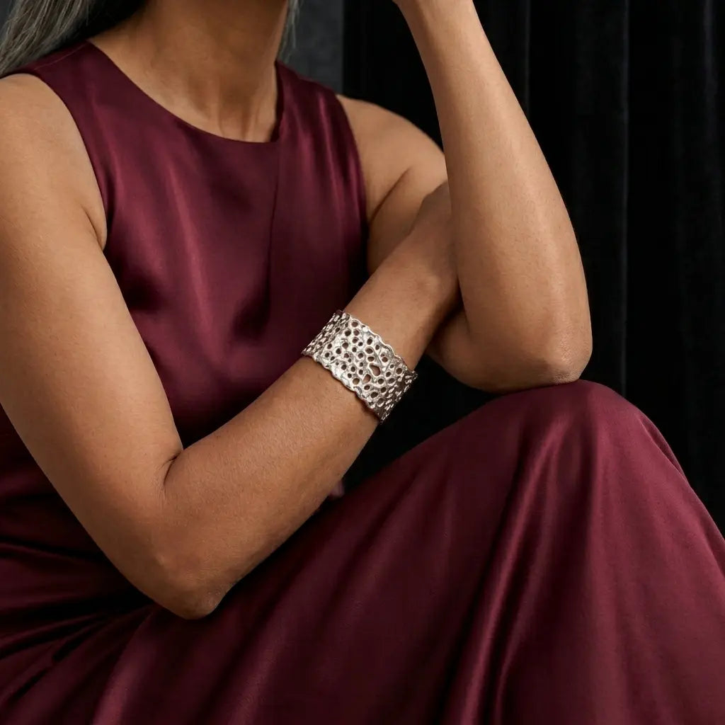 Model wearing a wide silver Origin Honeycomb cuff with an open textured pattern, styled with a wine-coloured dress.