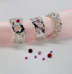 Three Origin silver rings with colourful gemstones arranged on a pink ribbon