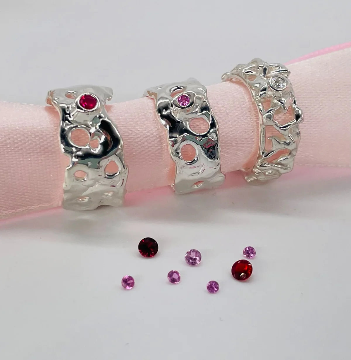 Three Origin silver rings with colourful gemstones arranged on a pink ribbon