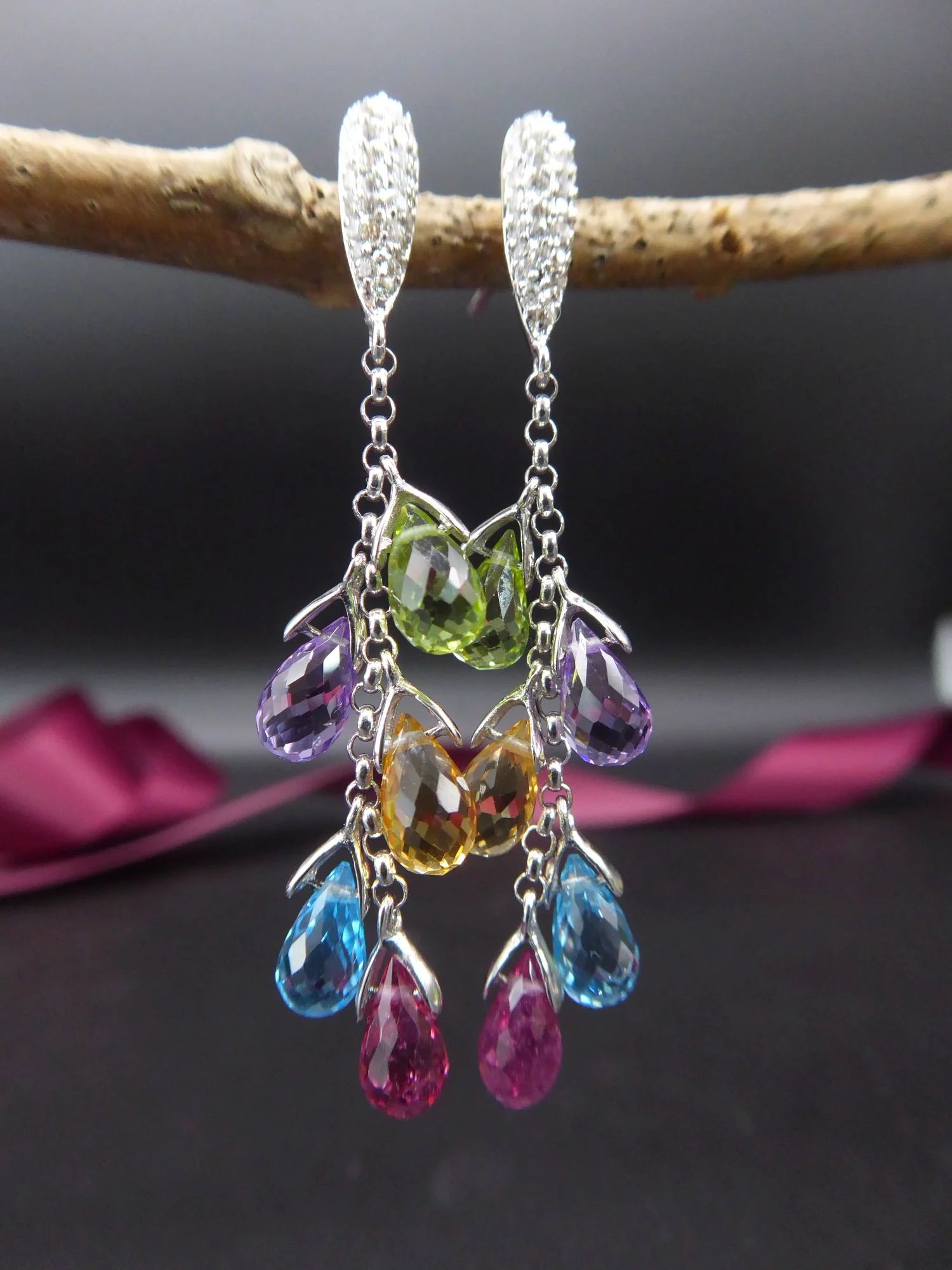 A pair of 18ct yellow gold drop earrings featuring clusters of pastel briolette gemstones and brilliant-cut diamonds dark background.