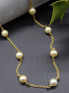 Ivory freshwater pearls spaced along an 18ct yellow gold chain necklace, arranged on a dark grey surface beside a green leaf.