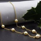Close-up of the pearl and gold chain necklace, showing lustrous ivory freshwater pearls and yellow gold links beneath holly leaves