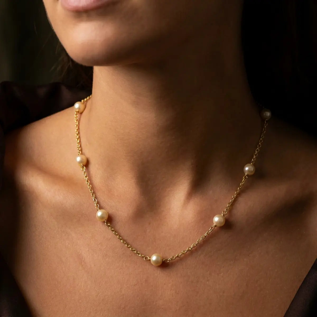 Model wearing a pearl and gold chain necklace with seven ivory freshwater pearls spaced along an 18ct yellow gold chain.