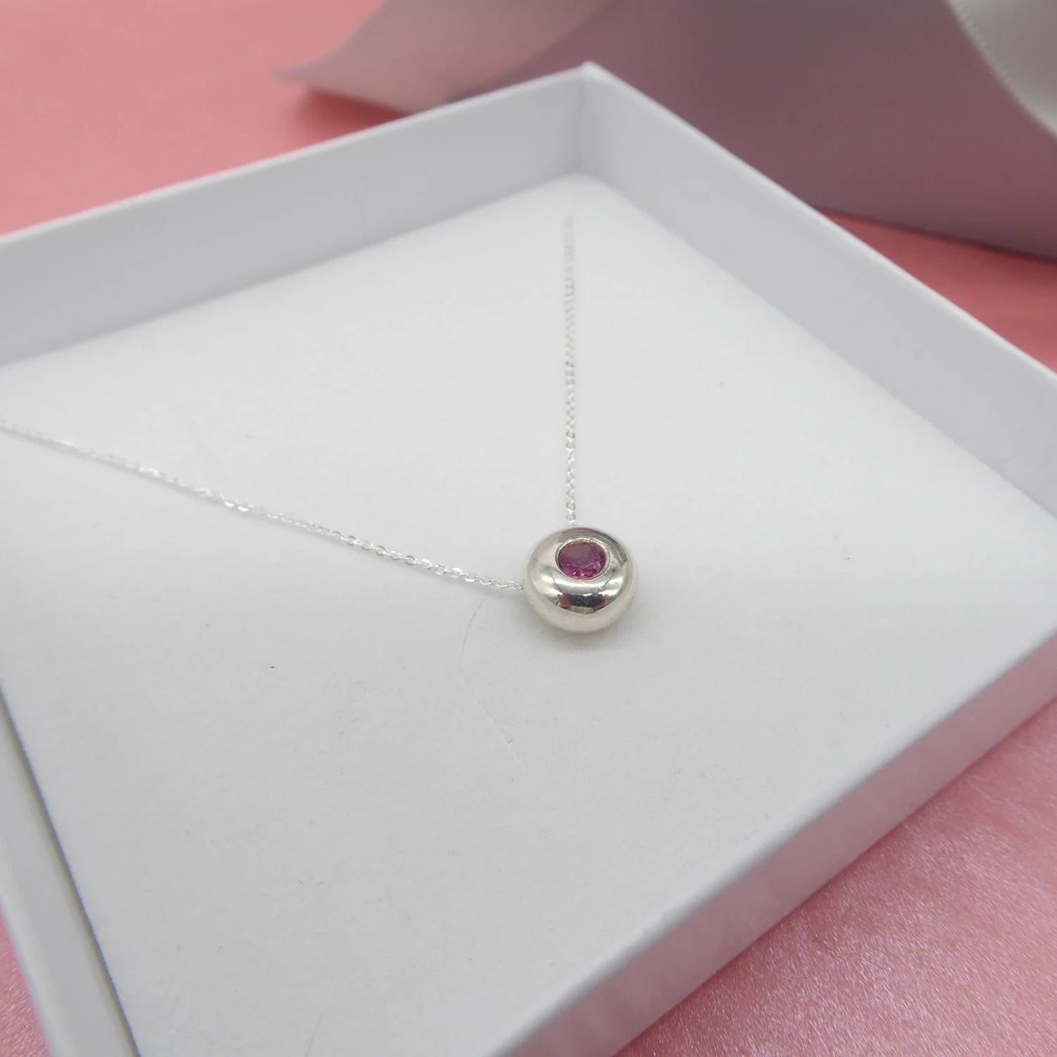 Silver slider necklace with a deep pink tourmaline gemstone pendant in a white box on a pink background