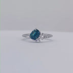 Selene oval teal sapphire and diamond asymmetric cluster engagement ring in 18ct white gold or platinum, rotating 360° studio video showing the vivid teal sapphire and diamond cluster, handmade in our London studio