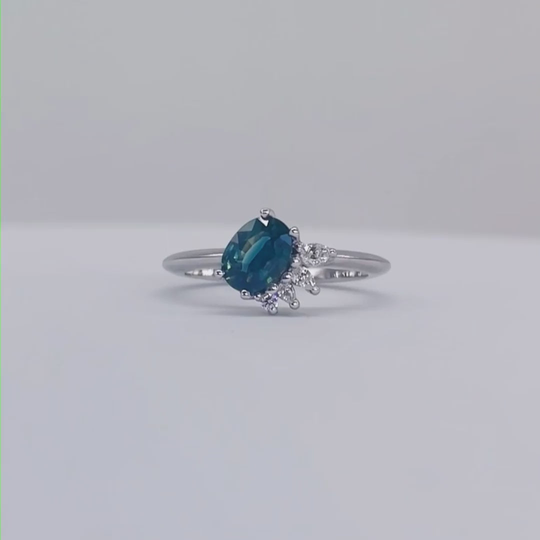 Selene oval teal sapphire and diamond asymmetric cluster engagement ring in 18ct white gold or platinum, rotating 360° studio video showing the vivid teal sapphire and diamond cluster, handmade in our London studio