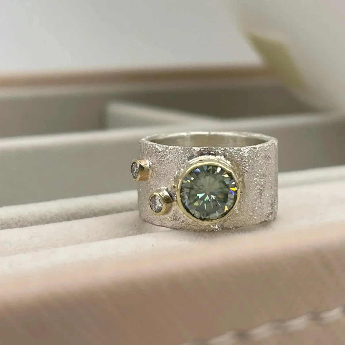 Close-up of the Rivda moissanite and diamond ring with a central moissanite and two diamond accents, displayed on a tray