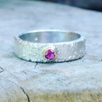 Silver textured ring with a ruby gemstone set in a gold setting.