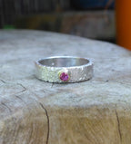 Silver textured ring with a ruby gemstone set in a gold setting on a wooden surface.