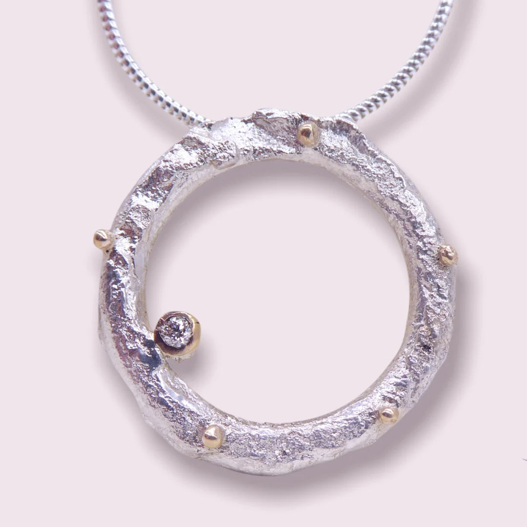 Close-up of the Rivda diamond loop pendant showing the organic hand-forged silver texture, gold beads and diamond set in the surface