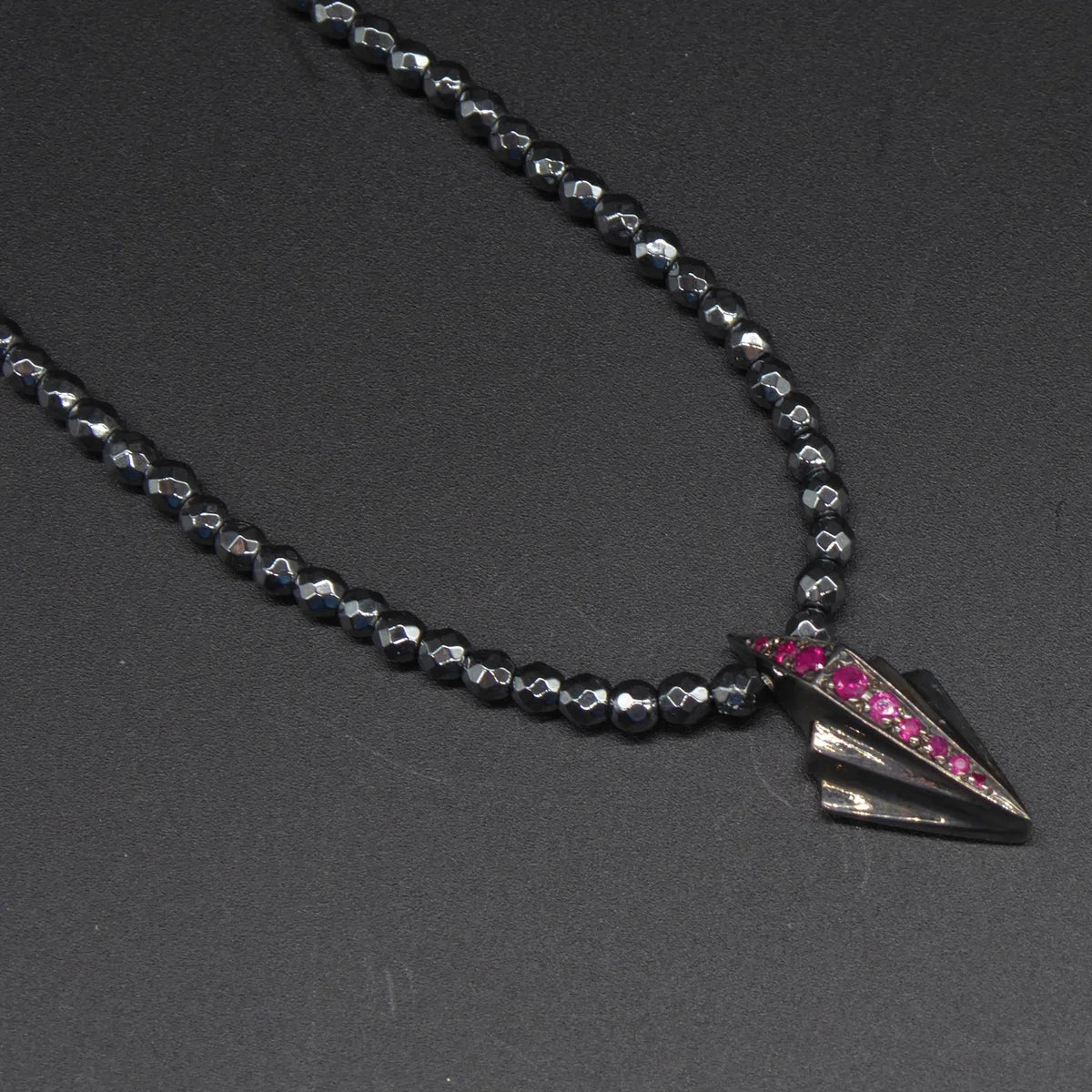 Close-up of Art Deco silver pendant set with rubies on faceted hematite bead necklace, angled view