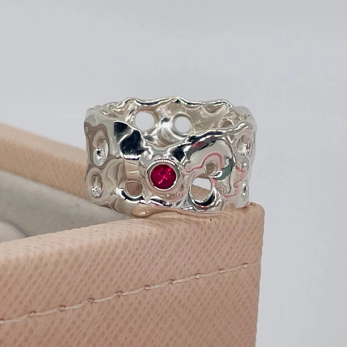 Origin Honeycomb Ring in sterling silver with a brilliant-cut ruby, shown on a beige jewellery box