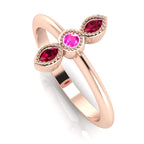 Angled perspective of an 18ct rose gold trilogy ring with a ruby and pink sapphires featuring fine milgrain textured edges.