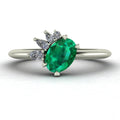 Selene cluster engagement ring, featuring a vibrant oval emerald nestled within an asymmetric white diamond arrangement on a white metal band.