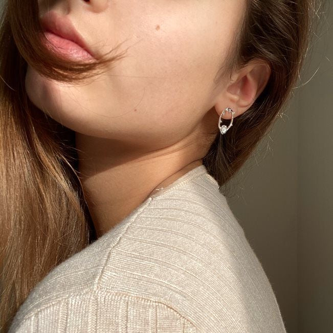 Model wearing a silver rose and thorn earring with an open oval design, styled with a cream ribbed top