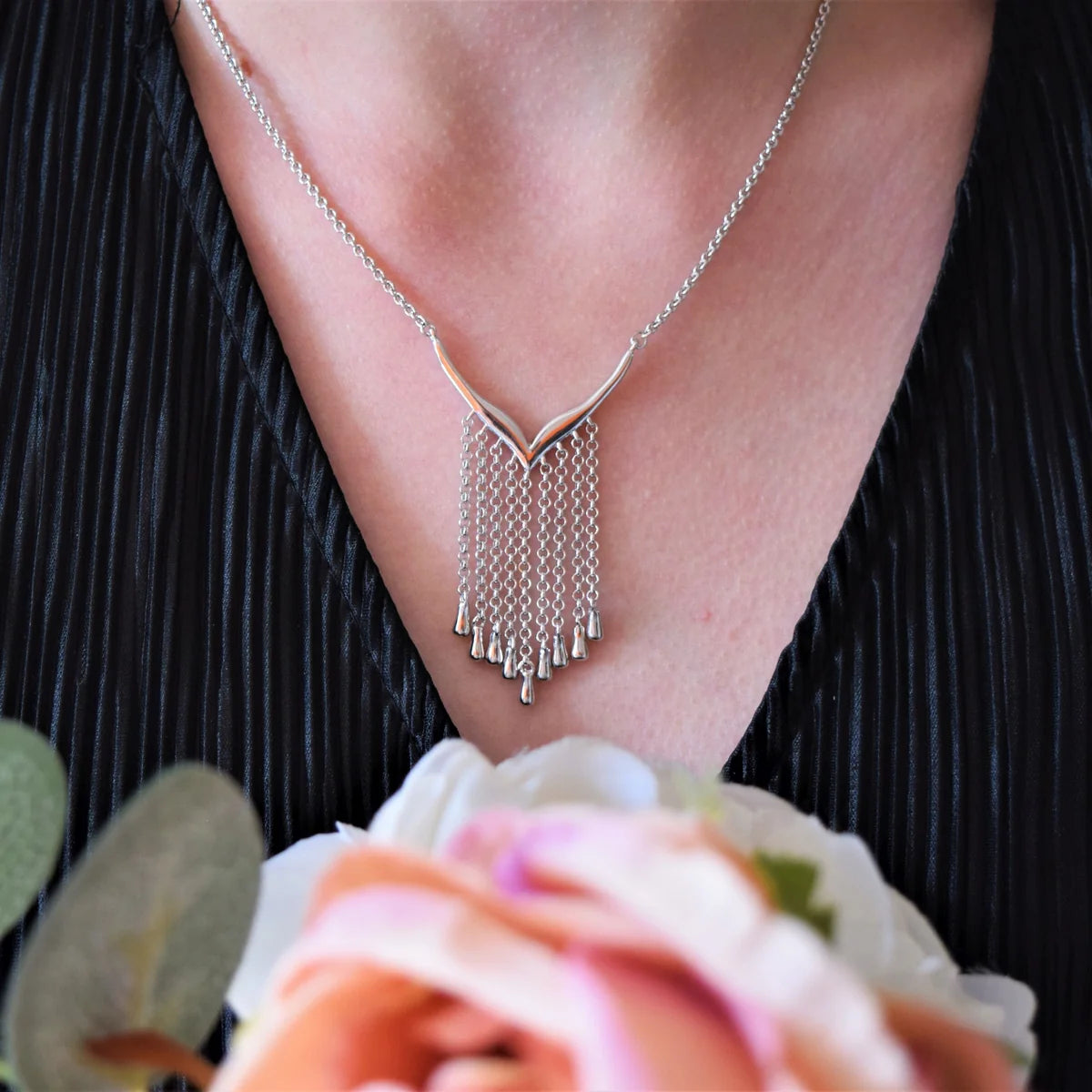Silver Waterfall Necklace worn with a black pleated top, showing its V-shaped centre and cascading silver droplet chains above pink flowers.