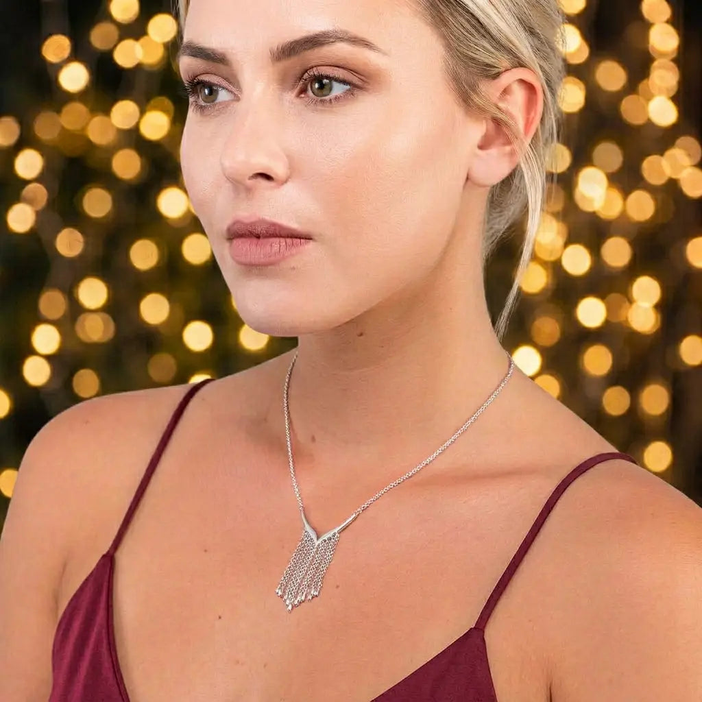 Model wearing a silver Waterfall necklace with a curved centrepiece and cascading chain fringe against a white background.